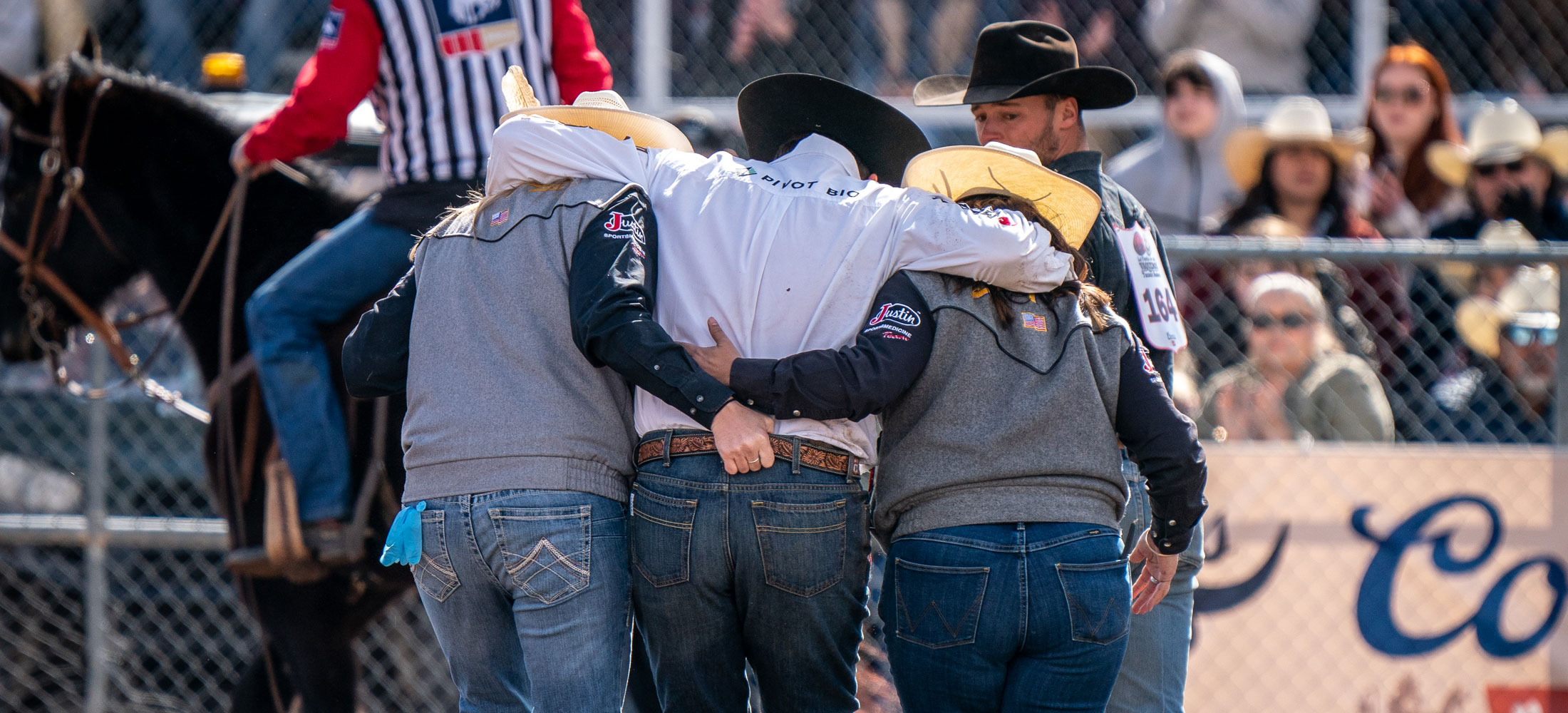 Two JST ladies and a steer wrestler, Jacob Edler, walking out of the arena, the two men holding the middle man helping him after an injury.